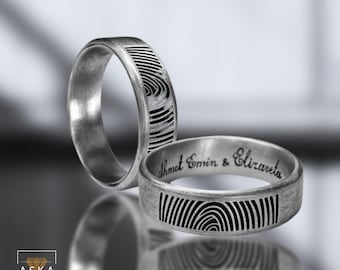 May include: Two silver wedding bands with fingerprint designs engraved on the outside. The band on the right has the inscription "Ahmet Emin & Elizaveta".