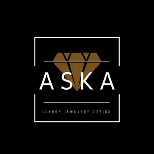 Op de afbeelding: Een logo op een zwarte achtergrond met het witte woord "ASKA", met daaronder "LUXURY JEWELRY DESIGN". Een bruine diamantvorm is gecentreerd boven de tekst, binnen een wit rechthoekig kader.