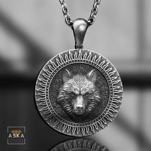 Op de afbeelding: Een zilveren ketting met een hanger met een wolfskop in een cirkelvormig ontwerp met een zonnestralenpatroon rond de rand.