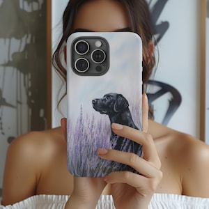Può includere: Una custodia per telefono con un ritratto di un cane Labrador Retriever nero in un campo di lavanda. La custodia ha uno sfondo bianco con un effetto acquerello.