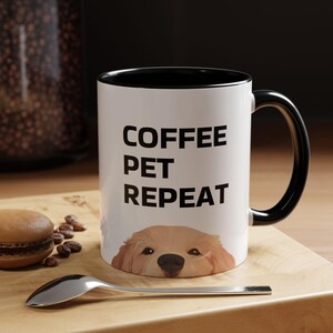 May include: White ceramic coffee mug with a black rim and handle. The mug has the text "COFFEE PET REPEAT" in black lettering. A golden retriever dog's head is peeking out from the bottom of the mug.