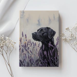 Puede incluir: Un cuaderno con una pintura de un perro labrador negro en un campo de lavanda. El perro está representado con un pelaje negro brillante y una mirada atenta. El fondo es una suave mezcla de colores, creando una impresión artística.