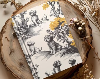 May include: A white notebook with a black and white illustration of dogs and trees. The dogs are in a variety of poses, and the trees have yellow leaves. The notebook is on a wooden surface.