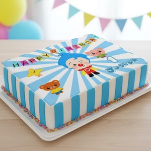 May include: A rectangular birthday cake with blue and white stripes, decorated with cartoon characters and the words "HAPPY BIRTHDAY" and "Joseph". The cake sits on a white tray and is decorated with colorful sprinkles.