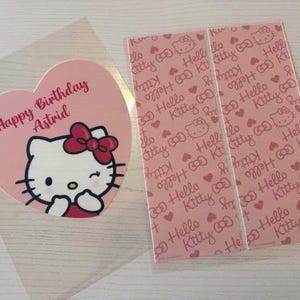 May include: A pink heart-shaped card with a Hello Kitty illustration and the text "Happy Birthday Astrid." Next to it are two pink rectangular cards with a repeating Hello Kitty pattern and the words "Hello Kitty."