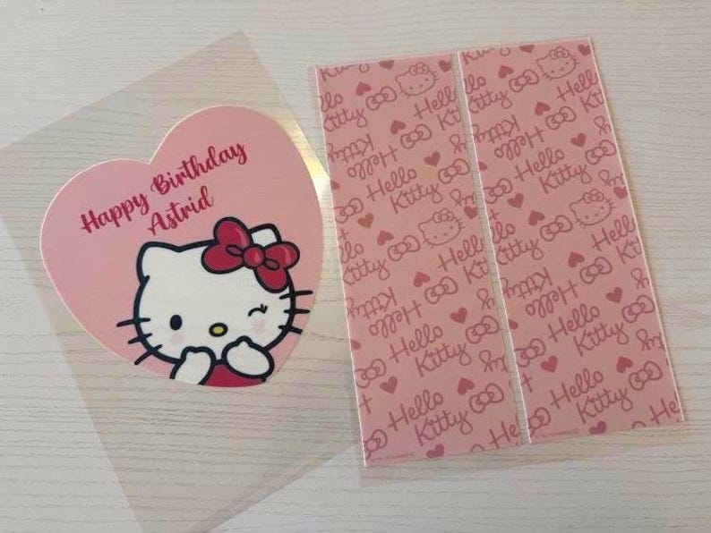 May include: A pink heart-shaped card with a Hello Kitty illustration and the text "Happy Birthday Astrid." Next to it are two pink rectangular cards with a repeating Hello Kitty pattern and the words "Hello Kitty."