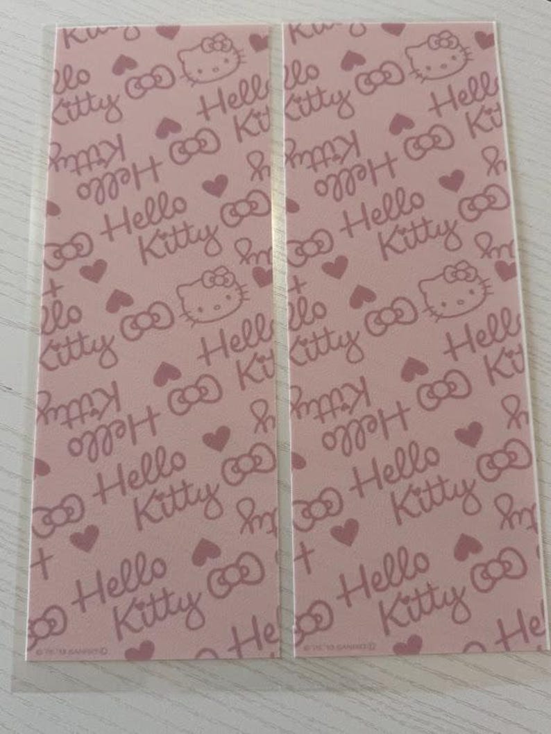 May include: Two pink Hello Kitty patterned cards. The cards feature a repeating pattern of Hello Kitty faces, bows, and hearts. The text "Hello Kitty" is also repeated throughout the design.