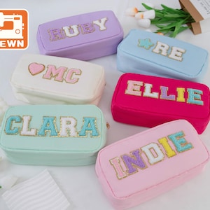 Puede incluir: Seis estuches con cremallera de colores con diferentes nombres bordados en ellos con letras de colores. Los nombres son Ruby, Wye, MC, Ellie, Clara e Indie.