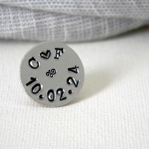 May include: A silver metal disc with the letters "C & F" and the date "10.02.14" engraved on it. The disc also has a small heart and a swirl design.