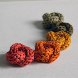 May include: A rainbow of colours in a row of knitted yarn knots. The knots are in shades of red, orange, yellow, brown, and grey.