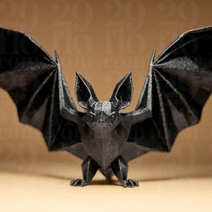Peut inclure: Sculpture de chauve-souris noire de style origami, ailes déployées. La chauve-souris présente un design géométrique avec des angles vifs et une surface texturée. Les ailes sont entièrement déployées, et la chauve-souris est debout.