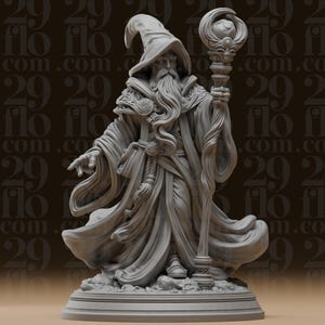 Op de afbeelding: Een grijs miniatuurbeeldje van een tovenaar in een lang, vloeiend gewaad en een puntmuts. Het figuur houdt een hoge staf met een bolvormige orb in de ene hand en heeft de andere hand naar voren uitgestoken. De tovenaar heeft een lange baard.
