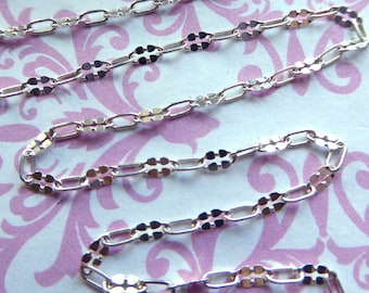 May include: Silver chain featuring a delicate, patterned design. The chain is made of small, oval-shaped links with a decorative detail on each link.