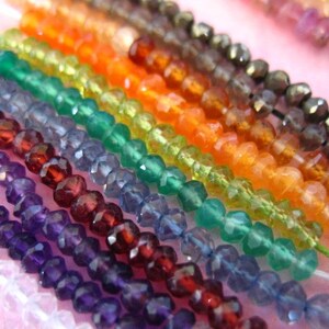 K&ouml;nnte beinhalten: Nahaufnahme von Str&auml;ngen facettierter Edelsteinperlen in verschiedenen Farben, darunter Amethyst, Granat, blauer Topas, gr&uuml;ner Aventurin, Karneol und Citrin. Die Perlen sind auf d&uuml;nnem wei&szlig;em Faden aufgef&auml;delt.