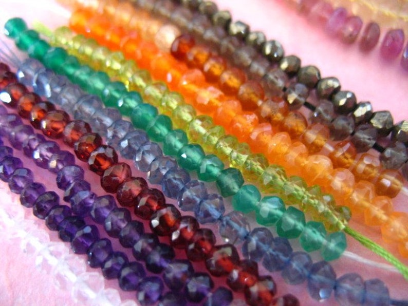K&ouml;nnte beinhalten: Nahaufnahme von Str&auml;ngen facettierter Edelsteinperlen in verschiedenen Farben, darunter Amethyst, Granat, blauer Topas, gr&uuml;ner Aventurin, Karneol und Citrin. Die Perlen sind auf d&uuml;nnem wei&szlig;em Faden aufgef&auml;delt.