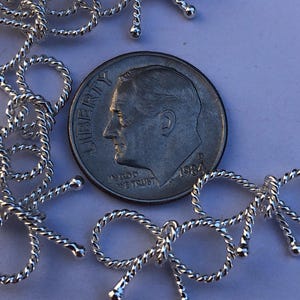 May include: Silver-toned metal bow-shaped charms, each with a twisted rope design. The charms are approximately the size of a US dime.