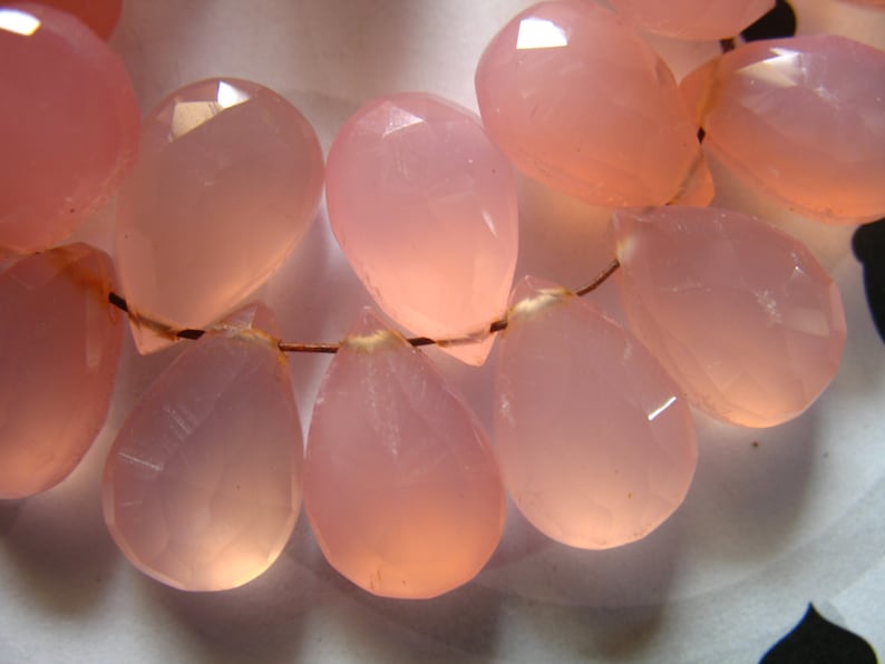 Puede incluir: Una hebra de cuentas de piedra preciosa de calcedonia rosa en forma de l&aacute;grima. Las cuentas est&aacute;n enhebradas en un alambre y son transl&uacute;cidas.