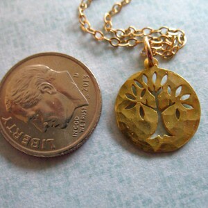 May include: Gold necklace with a tree of life pendant. The pendant is a round disc with a cut-out tree design. The chain is a delicate gold chain.