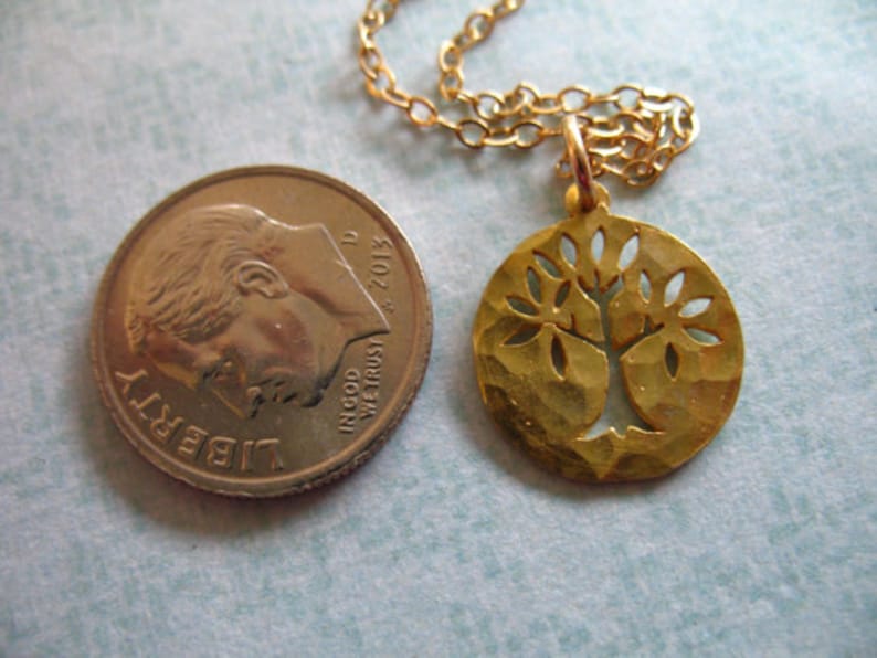 May include: Gold necklace with a tree of life pendant. The pendant is a round disc with a cut-out tree design. The chain is a delicate gold chain.