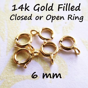 May include: Five 14k gold filled open jump rings, each measuring 6 mm in diameter. The rings are on a white background with a glittery texture.