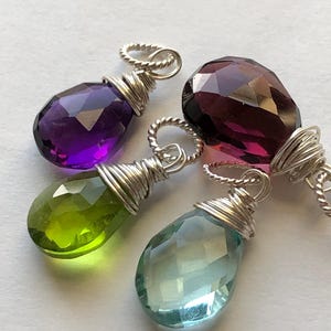 May include: Four gemstone pendants wrapped in silver wire. The gemstones are amethyst, green amethyst, aquamarine, and amethyst.