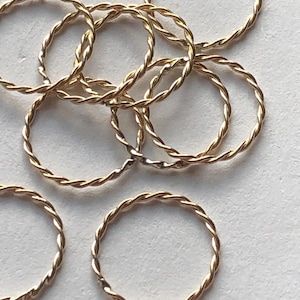May include: A group of gold-colored, twisted metal rings. The rings are all the same size and are arranged in a pile.