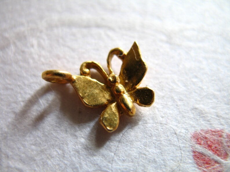 Puede incluir: Un dije de mariposa de color dorado con un bucle para sujetarlo a un collar o pulsera.