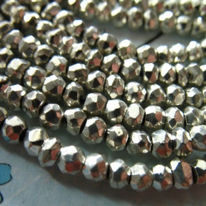 May include: A strand of silver-colored faceted beads. The beads are small and round, with a slightly irregular shape. They are strung together on a clear thread.