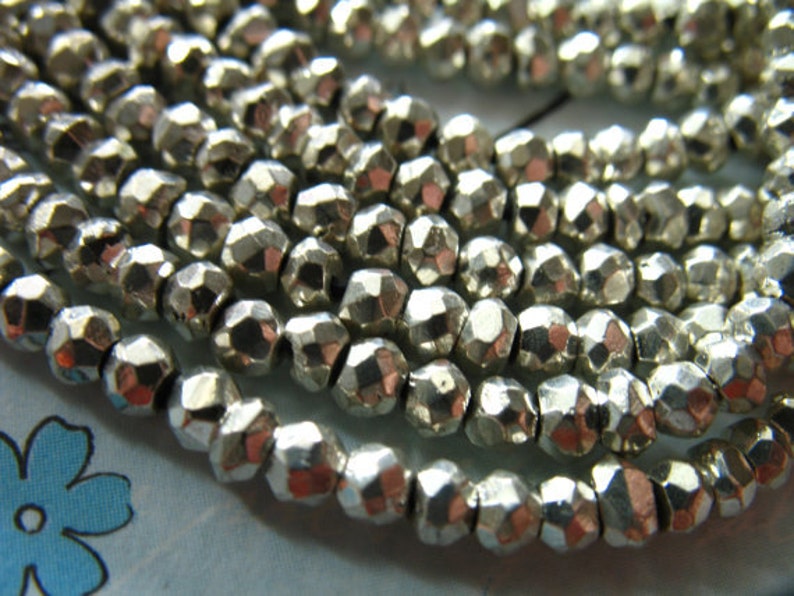 May include: A strand of silver-colored faceted beads. The beads are small and round, with a slightly irregular shape. They are strung together on a clear thread.