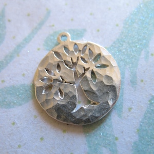 May include: Silver charm with a hammered texture and a cut-out design of a tree with leaves.