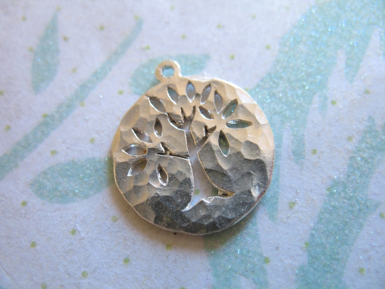 May include: Silver charm with a hammered texture and a cut-out design of a tree with leaves.