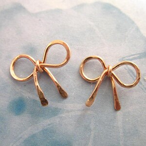 May include: A pair of rose gold bow earrings. The bows are made of wire and have a hammered texture.