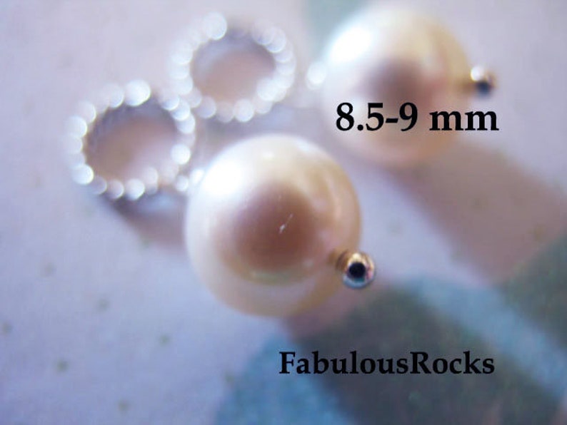May include: Two white pearl beads with silver jump rings, measuring 8.5-9 mm in diameter.