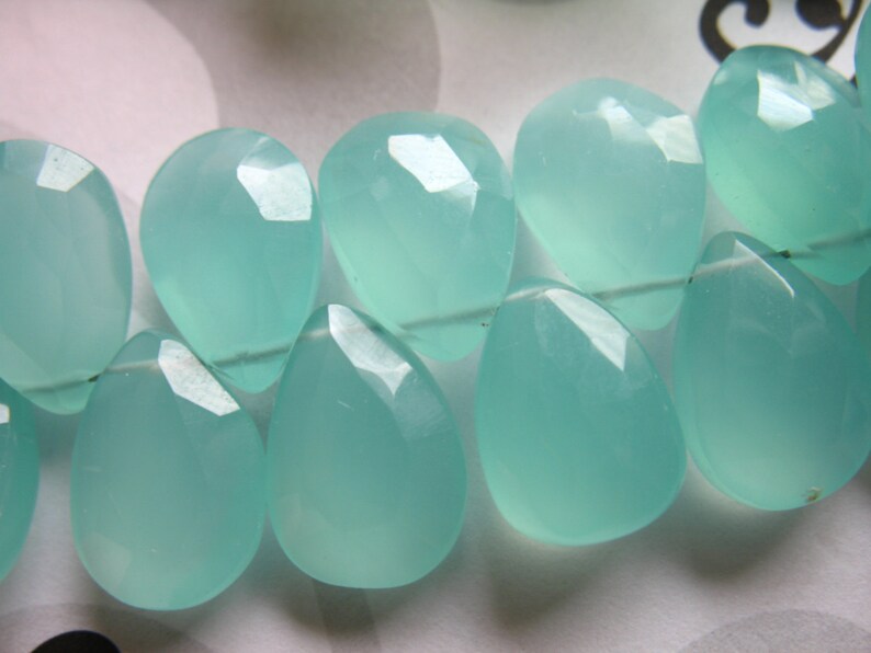 Pu&ograve; includere: Una collana di perle di pietra preziosa di forma a goccia di colore blu chiaro. Le perle sono lisce e lucidate, con un aspetto traslucido.