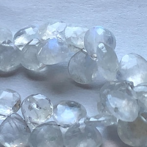 May include: A strand of iridescent white moonstone beads. The beads are faceted and have a pearlescent sheen.