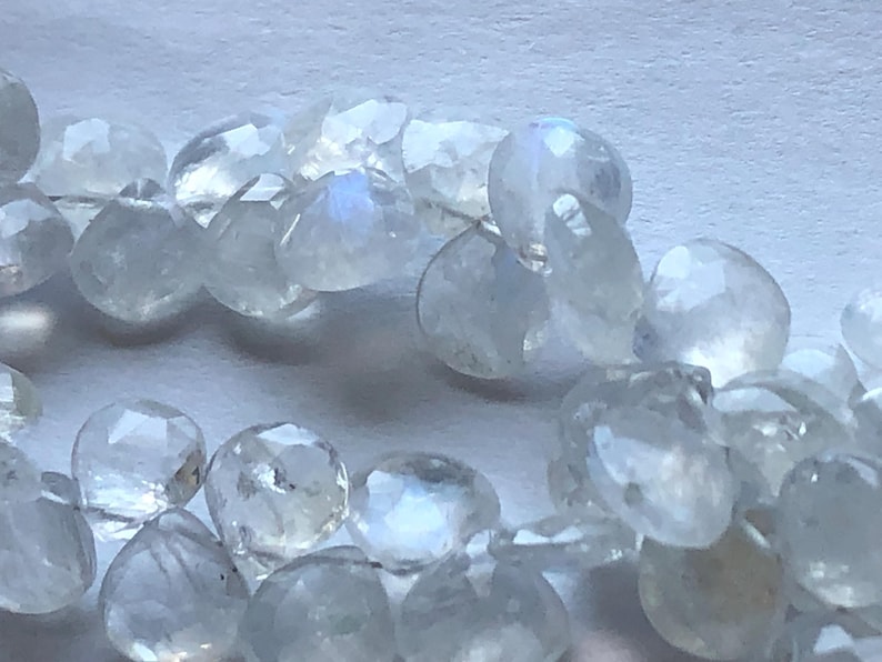 May include: A strand of iridescent white moonstone beads. The beads are faceted and have a pearlescent sheen.
