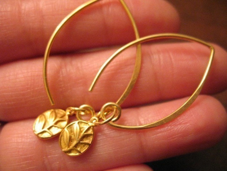 Puede incluir: Pendientes de oro con un delicado dise&ntilde;o de hojas. Los pendientes est&aacute;n hechos de alambre fino y tienen un estilo simple y elegante.