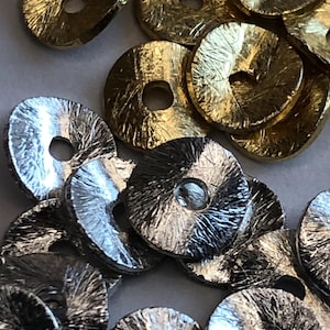 Peut inclure: Gros plan sur des perles métalliques dorées et argentées en forme de disque, à l'aspect texturé et martelé. Chaque perle a un trou central. Les perles sont éparpillées, suggérant qu'elles sont destinées à l'artisanat ou à la bijouterie.