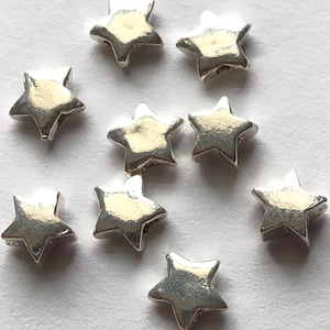 May include: Eight silver star-shaped beads with a hole in the centre for stringing.