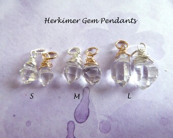 Op de afbeelding: Drie Herkimer-diamant hangers in verschillende maten, gelabeld S, M en L. Elke hanger is gewikkeld in goud- en zilverdraad en heeft een helder, facetgeslepen kristal.