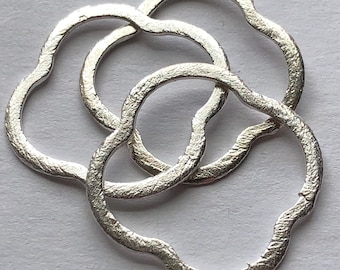 May include: Three silver rings with a wavy, organic shape. The rings are interlocked and have a textured surface.