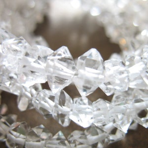 May include: A strand of clear quartz crystal beads, each bead is faceted and has a diamond-like shape.