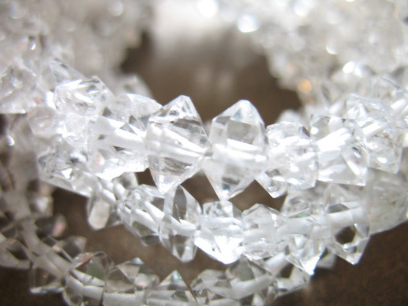 May include: A strand of clear quartz crystal beads, each bead is faceted and has a diamond-like shape.