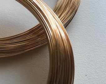 May include: A close-up of two spools of gold-colored wire. The wire is wound tightly around each spool, creating a smooth, shiny surface.