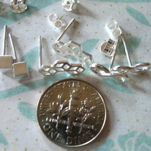 May include: A set of silver earrings with different designs, including a square, a honeycomb pattern, and an infinity symbol. The earrings are shown next to a US dime for scale.