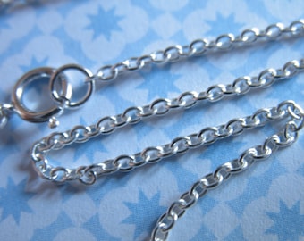 May include: A silver chain necklace with a lobster clasp. The chain is made of small, linked oval shapes.