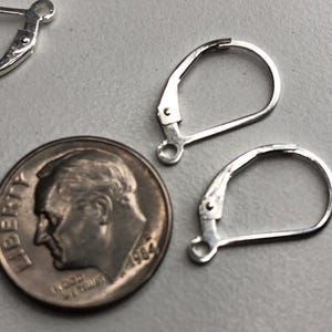 May include: Two silver earring hooks, one on top of the other, next to a 10 pence coin. The coin is dated 1984.