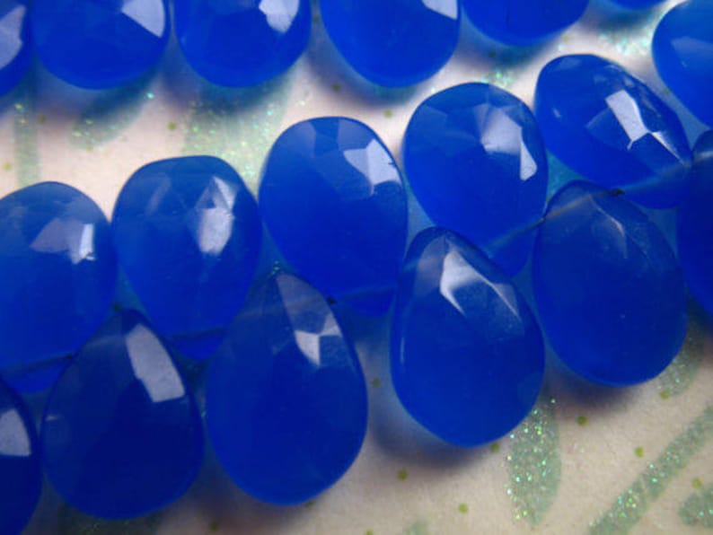Puede incluir: Una hebra de cuentas de piedras preciosas de color azul brillante, cada cuenta est&aacute; facetada y tiene forma de l&aacute;grima. Las cuentas est&aacute;n enhebradas en un hilo transparente.