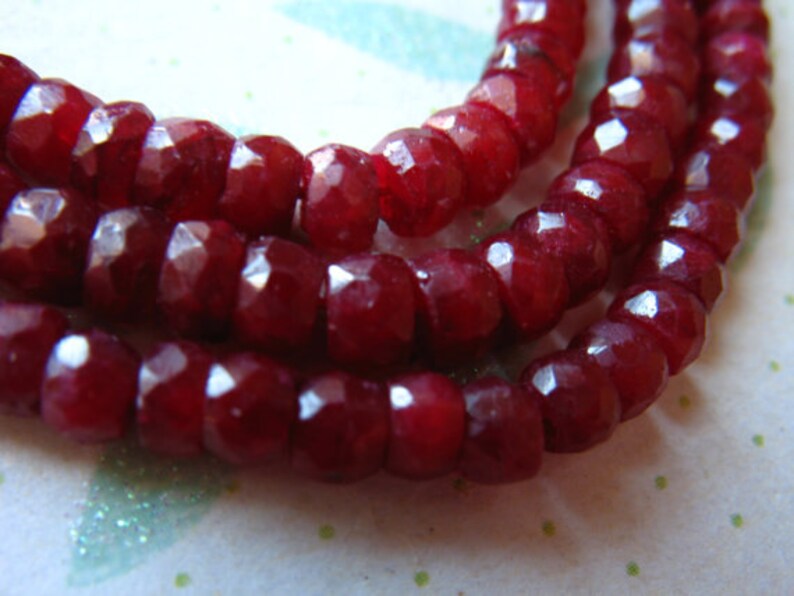 Puede incluir: Una hebra de cuentas de piedras preciosas facetadas de color rojo intenso. Las cuentas son redondas y tienen un acabado liso y pulido.