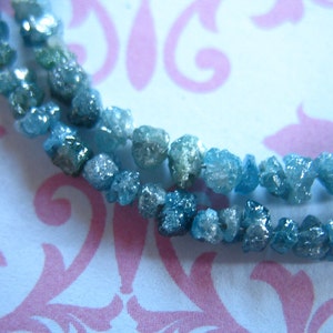 Puede incluir: Una hebra de diamantes en bruto azules y verdes, tambi&eacute;n conocidos como diamantes en bruto, sobre un fondo blanco con un patr&oacute;n floral rosa.